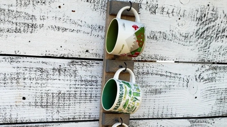A close up of mugs hanging from a vertical wall-mounted mug rack.
