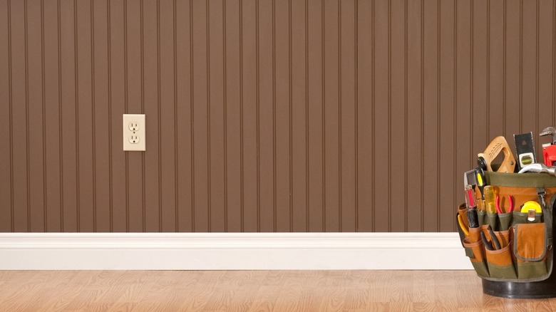 Tool bag sitting in front of brown beadboard wall with outlet