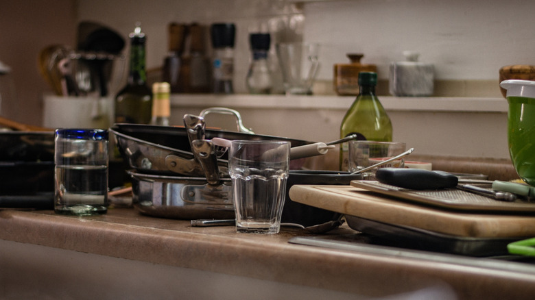 Cluttered kitchen island with piles of pans, dishes, and untensils