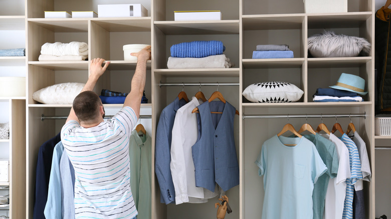 A man stretches to reach a box high up in a closet.