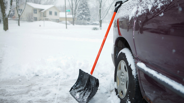 Snow shovel leaning on car in snowy driveway