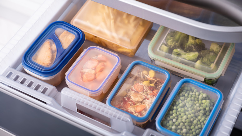 An open freezer drawer showing lots of food-filled plastic containers neatly stacked