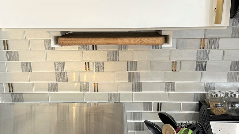 White brackets hold a wooden cutting board underneath the upper cabinets in a kitchen