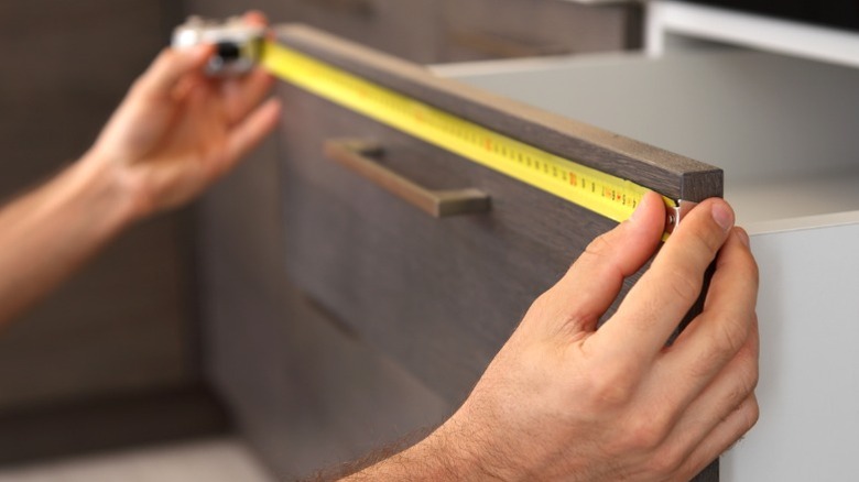 Person measuring dark wood kitchen drawer width