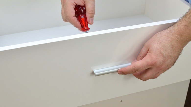 Person installing pull on a white drawer