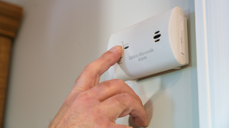 A person hitting the test button on a carbon monoxide detector