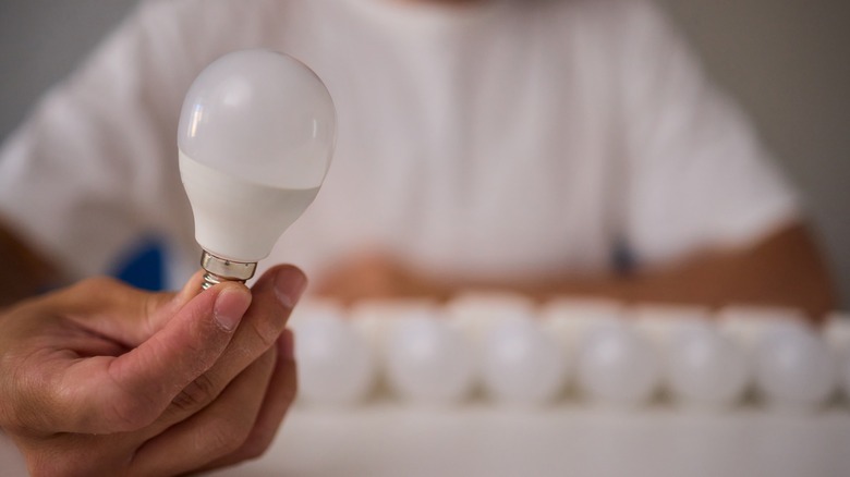 An up-close image of a man holding an LED bulb with a blurry background.