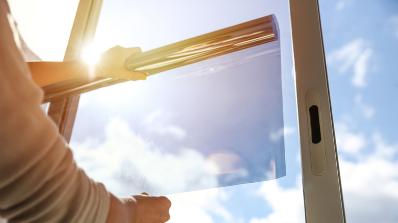 A person applying tinted window film to the inside of a window.
