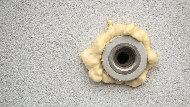 Close-up of a wall pipe opening sealed with expanding foam