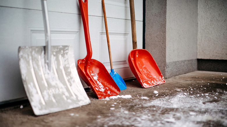 Different types of snow shovels lined up against the garage door.