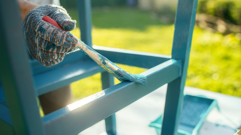 hand painting a wooden shelf with aqua paint outside