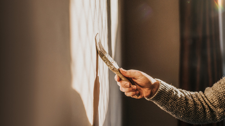 Light shines onto a wall being painted with a small brush