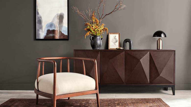 A modern chair and credenza topped with decorative items sit in front of a wall painted with Sherwin-Williams Urbane Bronze
