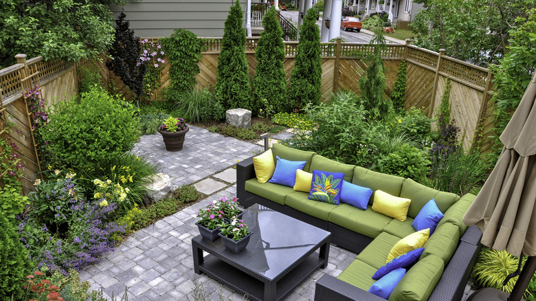 A beautiful small, urban backyard garden with a paver patio and trees, shrubs, and perennials.