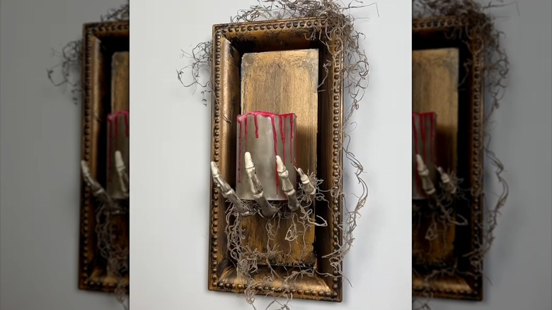 DIY Halloween wall sconce with skeleton hand holding a LED candle dripping with red wax and moss