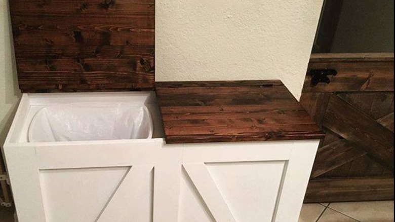 white cabinet with brown countertops opened with trash cans inside