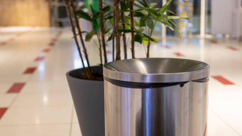 large steel trash bin behind large flower pot