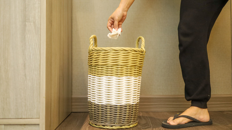 someone throwing tissue into a hamper trash can