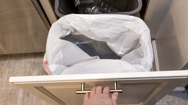 someone pulling a drawer out with two trash cans inside