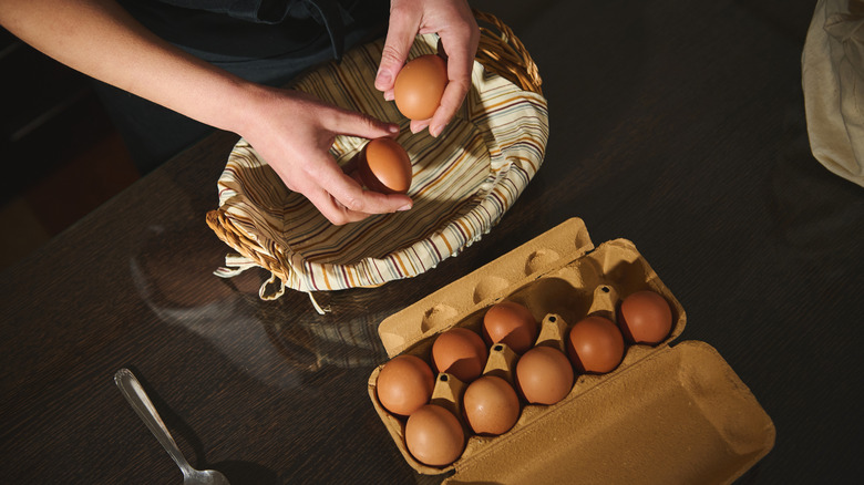 a female placing brown eggs from a carton into a lined basket