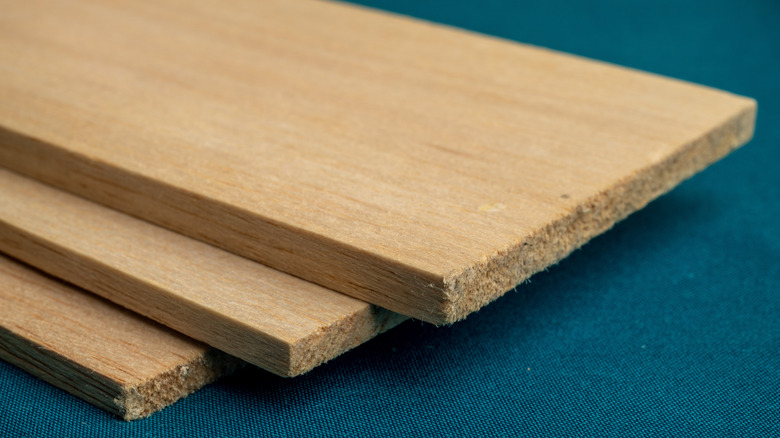 Three boards of balsa wood stacked on top of each other on a dark teal fabric background
