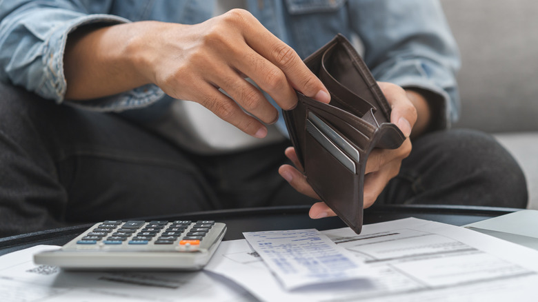 A person with bills and a calculator on a table in front of them opens their wallet