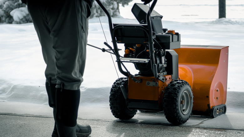 A person exits a storage space with a snowblower to clear a snowy driveway