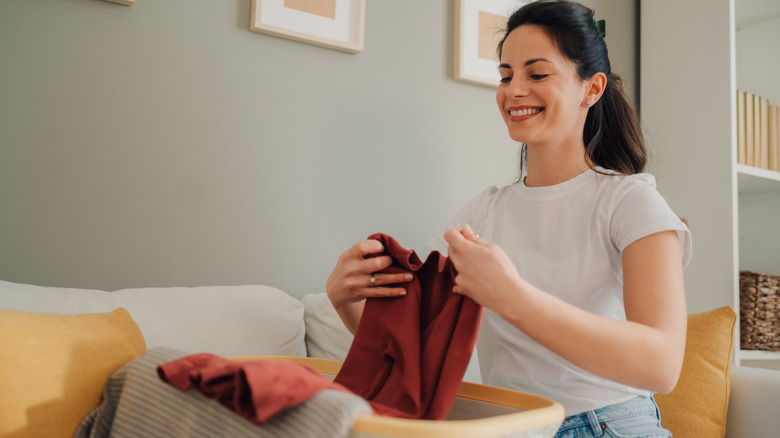 A smiling woman organizes items in a living room.