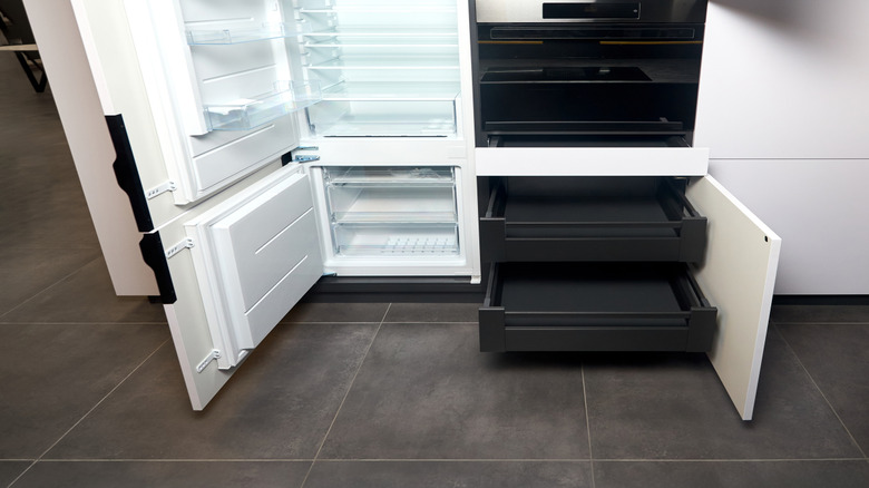 An integrated refrigerator is place among white kitchen cabinetry and a black oven
