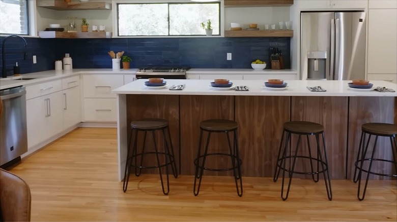 White kitchen with light wood floors, dark wood kitchen island, white cabinets, and a blue backsplash.