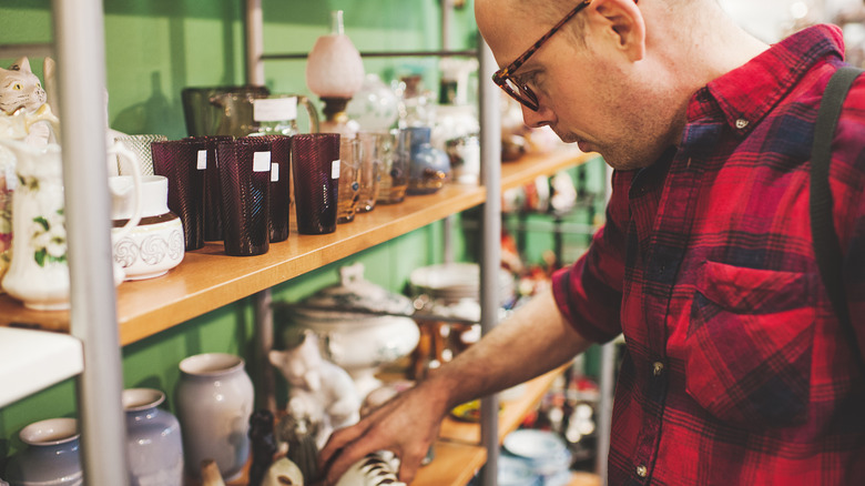 A man in a thrift store looks at home decor items on a display shelf.