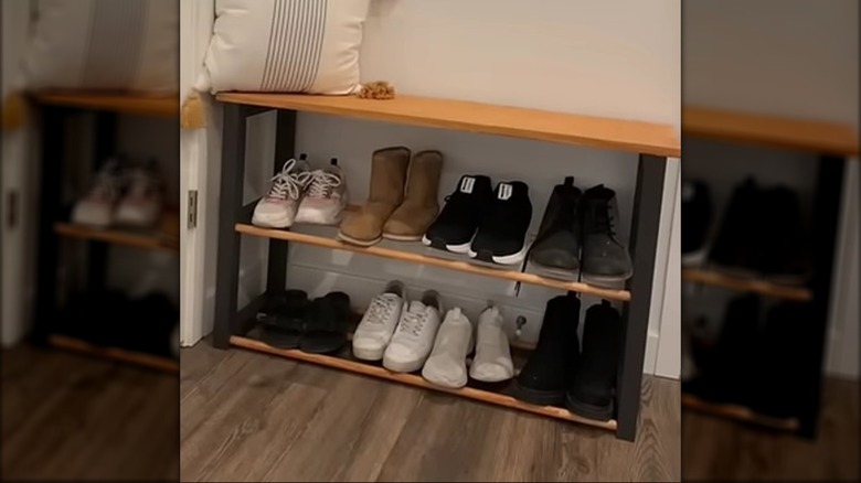 DIY shoe rack sits in entryway with eight pairs of shoes and a white pillow on top
