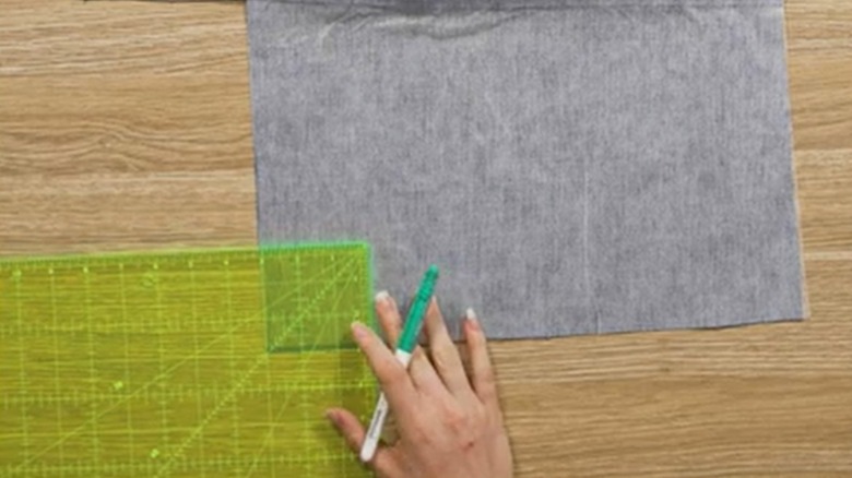 A hand holding a marker places a measuring tool on fabric.