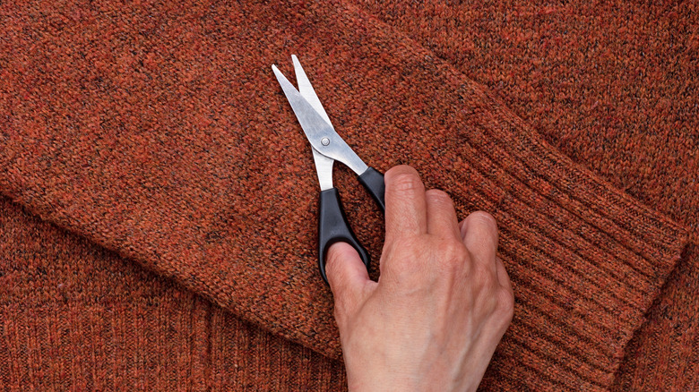 A hand holding scissors rests on an orange sweater sleeve.