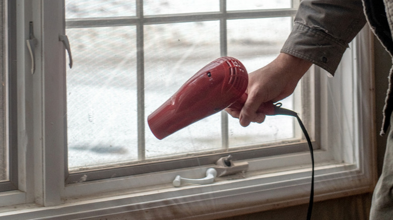 Man holding hair dryer and using it to install plastic film in window
