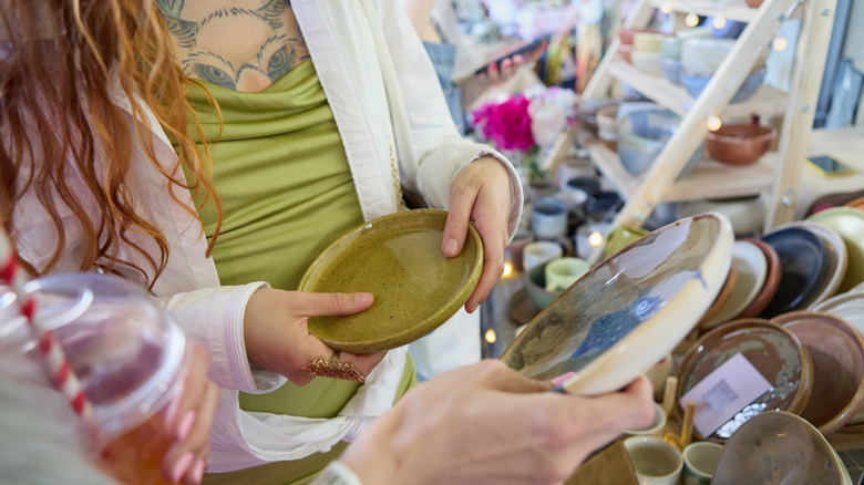 Two people hold vintage ceramic plates at a thrift shop
