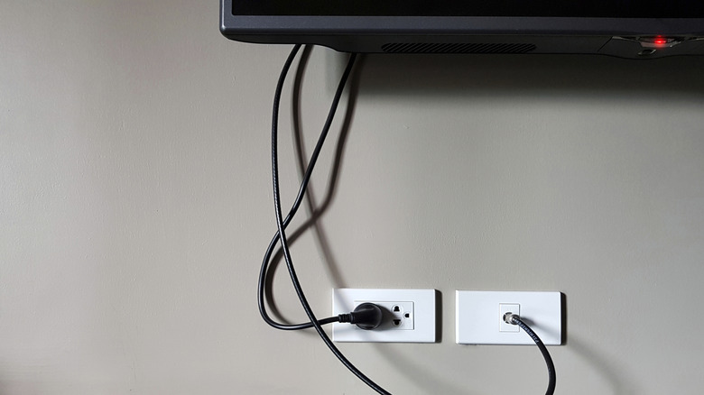 A TV hanging on a white wall with a cord hanging down.
