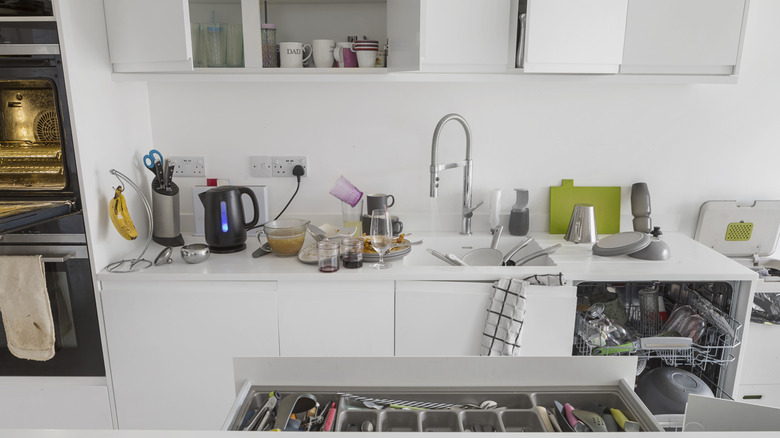 A white, cluttered kitchen with dishes and other items on the counter.