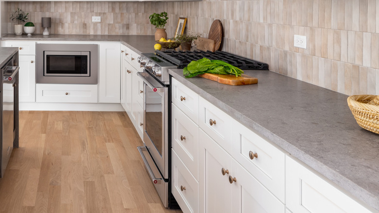 Sand and stone kitchen with gray quartz countertops, white cabinets, and a vertical tile backsplash.