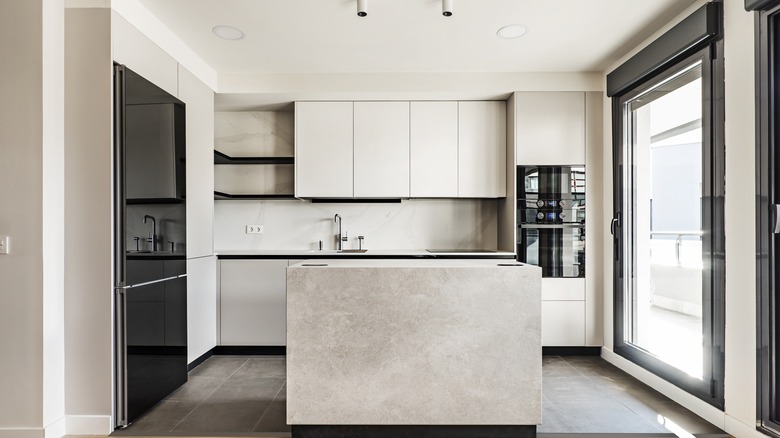 A kitchen white white cabinetry and pale gray marble island