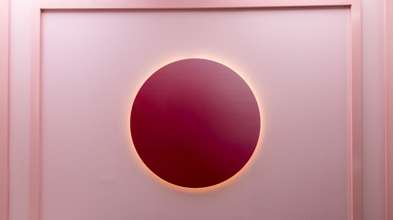 A raspberry pink circular light in the center of a light pink wall