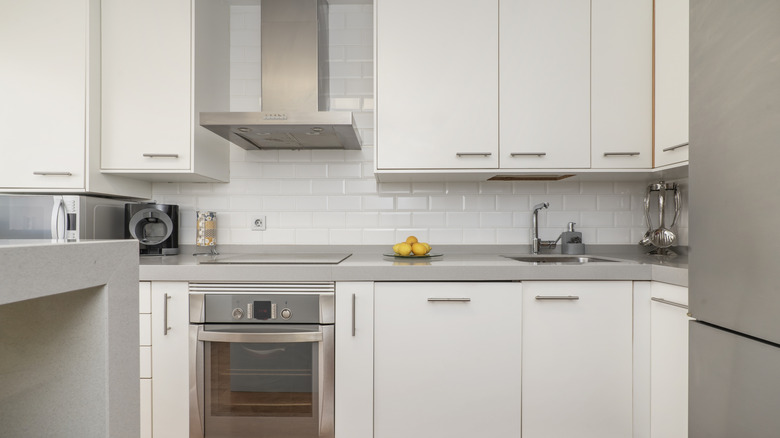 A modern small kitchen with a reflective white tile backsplash, grey countertops, and stainless steel appliances.