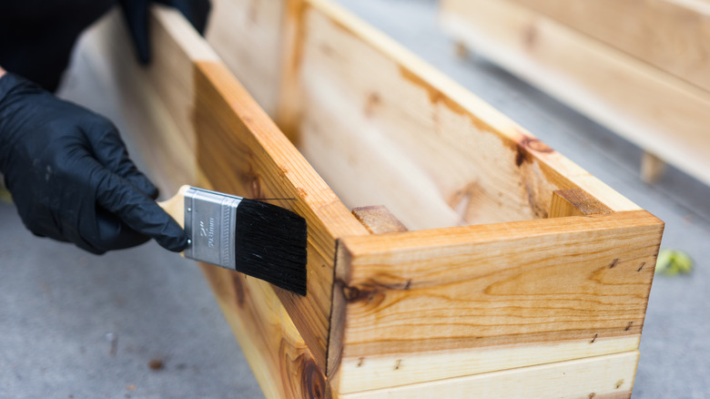 A gloved hand applies sealant to a wood garden planter.