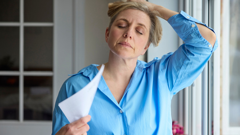 Woman fans herself with a piece of paper in a home near a window
