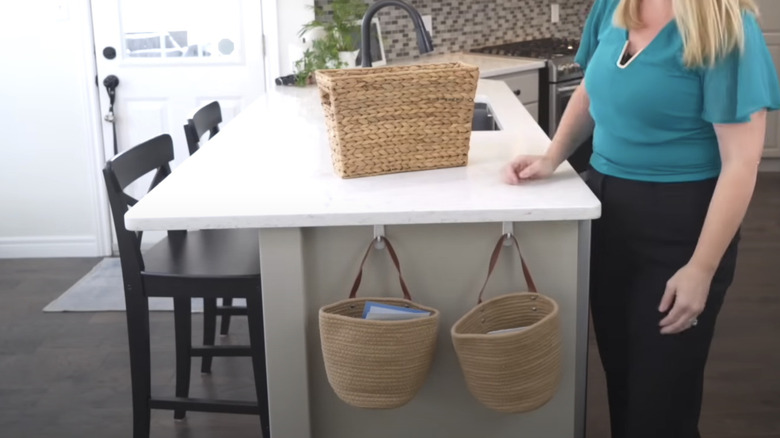 A woman standing beside kitchen table with two hanging baskets attached to it to keep countertops clear