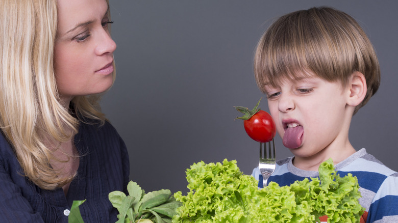 Mother trying to feed her little son who hates eating tomato