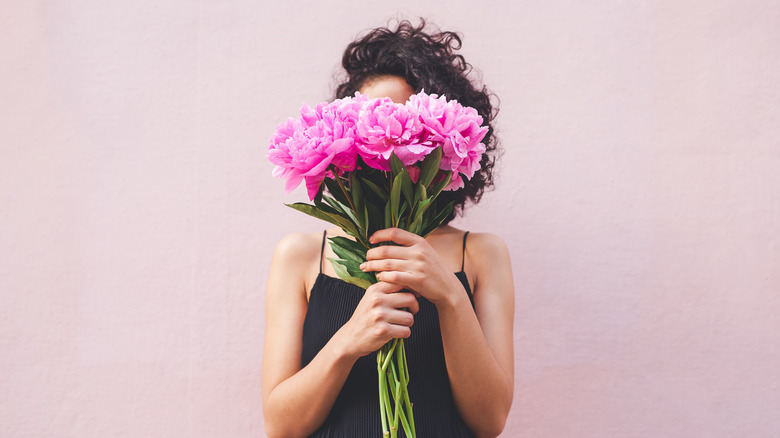 Woman holds peonies in front of her face
