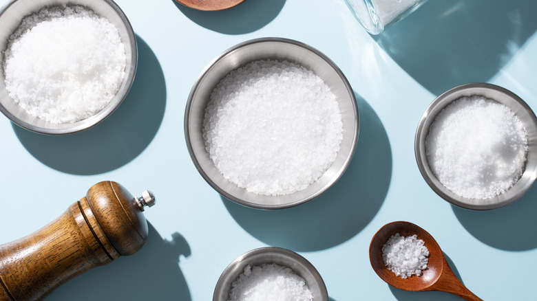 Various types of salt displayed in small bowls with a pepper grinder on the side