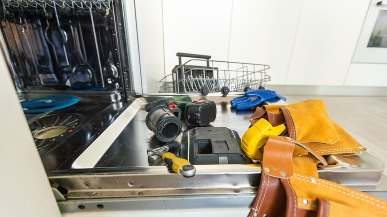 Tools resting on an open dishwasher door for repairs