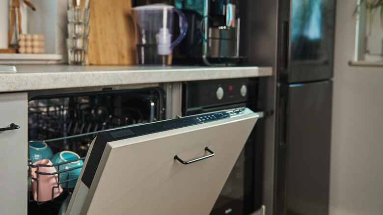 A dishwasher propped open with dishes inside
